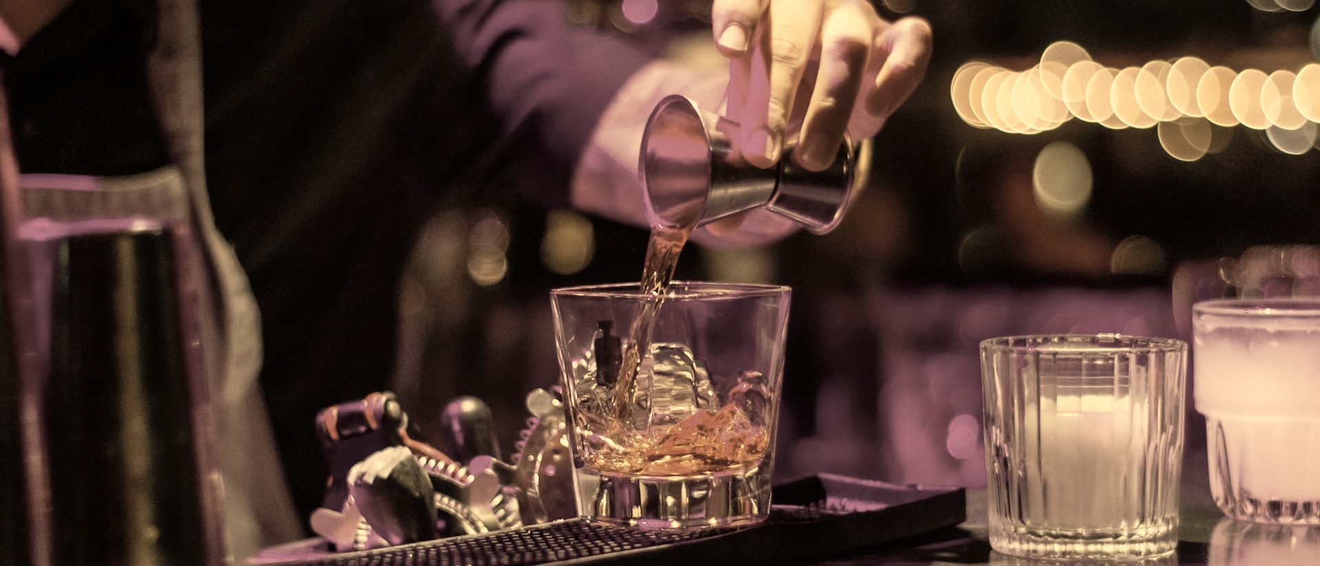 A bartender measuring a pour into a glass over ice during service.